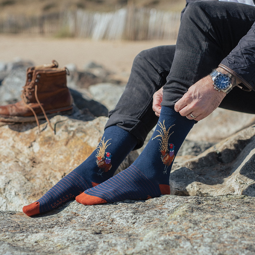 Person mit blauen Motivsocken und Sportschuhen sitzt entspannt auf einem Holzsteg am See